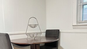 Un coin repas avec une table ronde, deux chaises noires et une étagère en fil de métal.