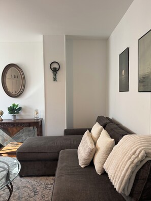 Una sala moderna con un sofá modular, una mesa de centro de vidrio y un tapiz decorativo.