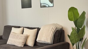 Un canapé gris agrémenté de coussins blancs à texture, un pot de fleurs en osier et deux œuvres d’art encadrées accrochées au mur.