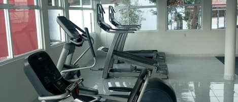 Uma academia com equipamentos de ginástica, janelas amplas e um piso de azulejos limpo.