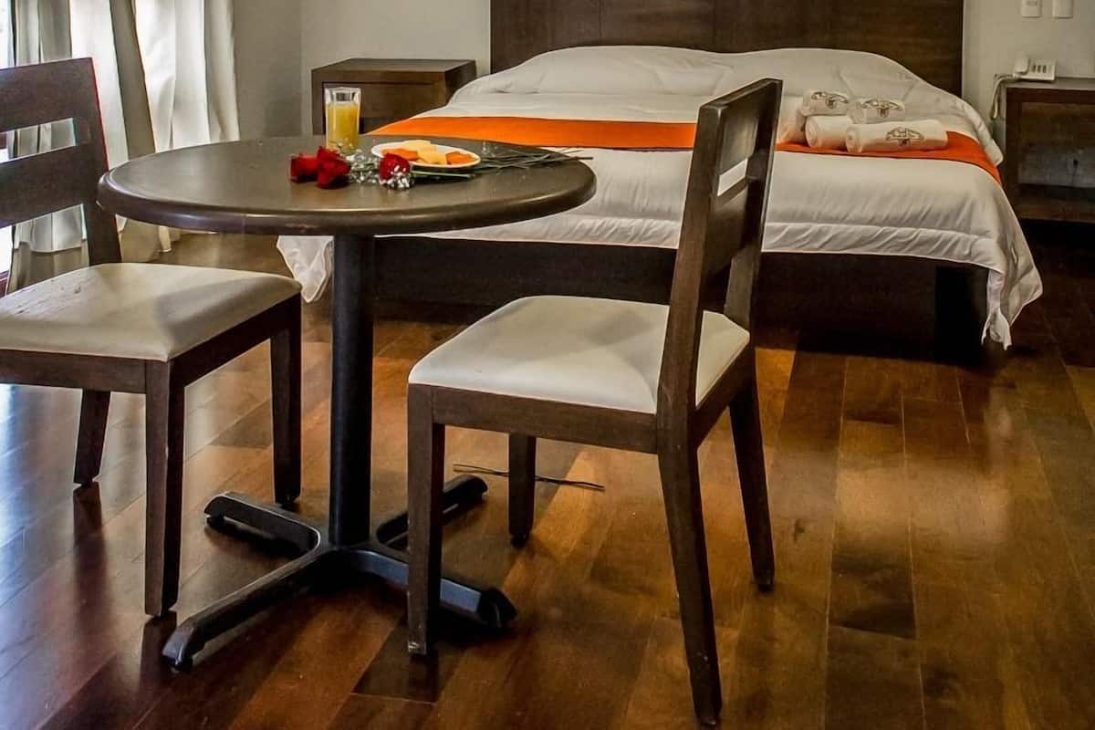 Une chambre d’hôtel avec un lit, une table ronde avec deux chaises, une petite table avec un verre de jus d’orange et une table de chevet avec une lampe.