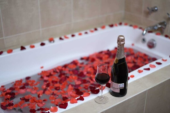 Une baignoire remplie de pétales de rose et une bouteille de vin.