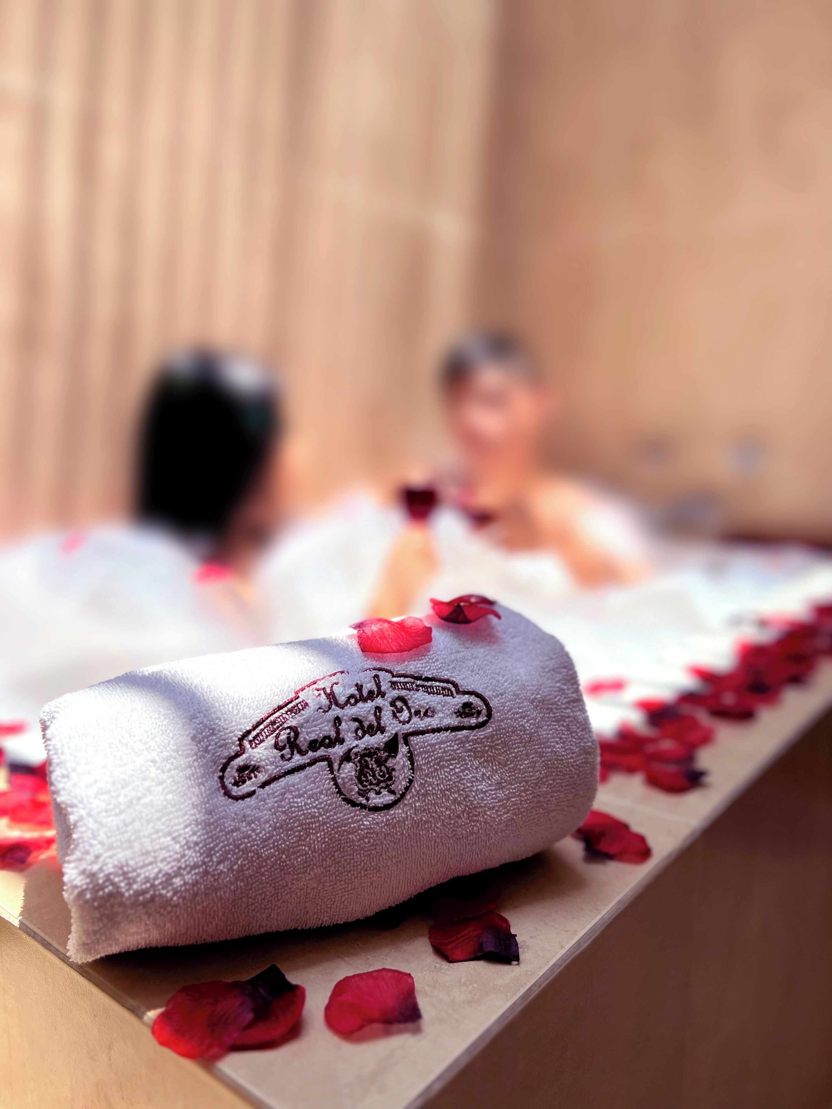 A towel with embroidered text and rose petals on a wooden surface.