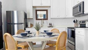 Una cocina moderna con armarios blancos, electrodomésticos de acero inoxidable y un comedor con sillas de mimbre y una mesa redonda.