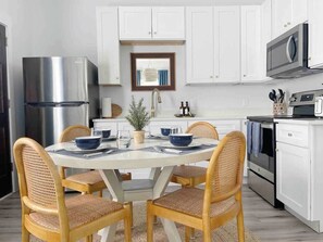 A modern kitchen with white cabinets, stainless steel appliances, and a dining area with wicker chairs and a round table.