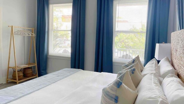 Habitación de hotel con una cama grande, cortinas azules, un perchero de madera y vistas al exterior.