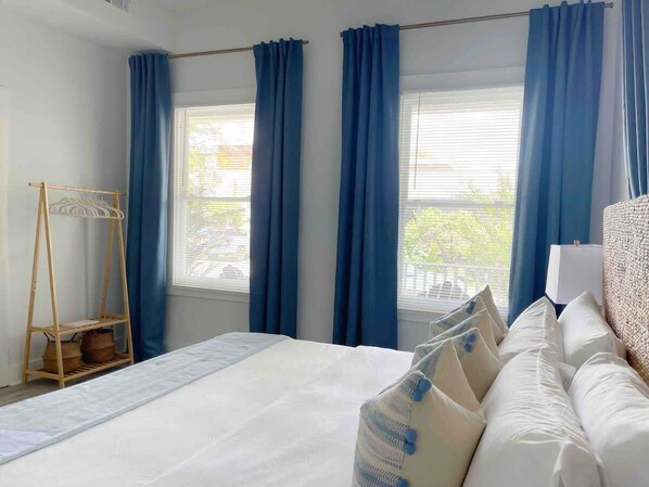 A hotel room with a large bed, blue curtains, a wooden rack, and a view of the outside.