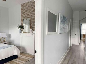 A bedroom with a bed, a dresser, a mirror, and a brick wall.