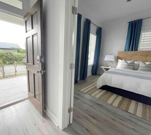 A hotel room with a bed, a nightstand, a lamp, and a view of the outdoors.