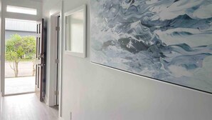 Un pasillo con un cuadro abstracto de gran tamaño en la pared, una puerta que da al exterior y vistas a un jardín.