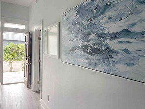 A hallway with a large abstract painting on the wall, a door leading outside, and a view of a garden.