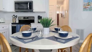 Un comedor con una mesa redonda, armarios blancos, microondas y una planta en maceta.