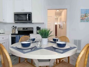 A dining area with a round table, white cabinets, a microwave, and a potted plant.