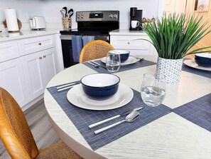 A dining area with a round table set for two, featuring a blue bowl, a glass of water, and cutlery.