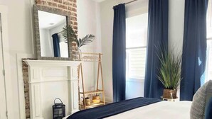 Une chambre à coucher avec un lit, une commode, un miroir, une fenêtre avec des rideaux et une plante.