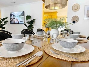 Mesa de jantar posta com pratos, tigelas e talheres brancos, em volta de jogos americanos de tecido.