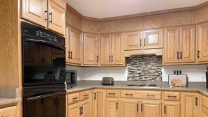 Una cocina con armarios de madera, un horno negro, un tostador y un salpicadero de azulejos.