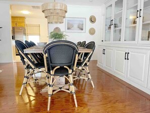 A dining area with a wooden table and wicker chairs, a white cabinet with glass doors, and a hanging light fixture.