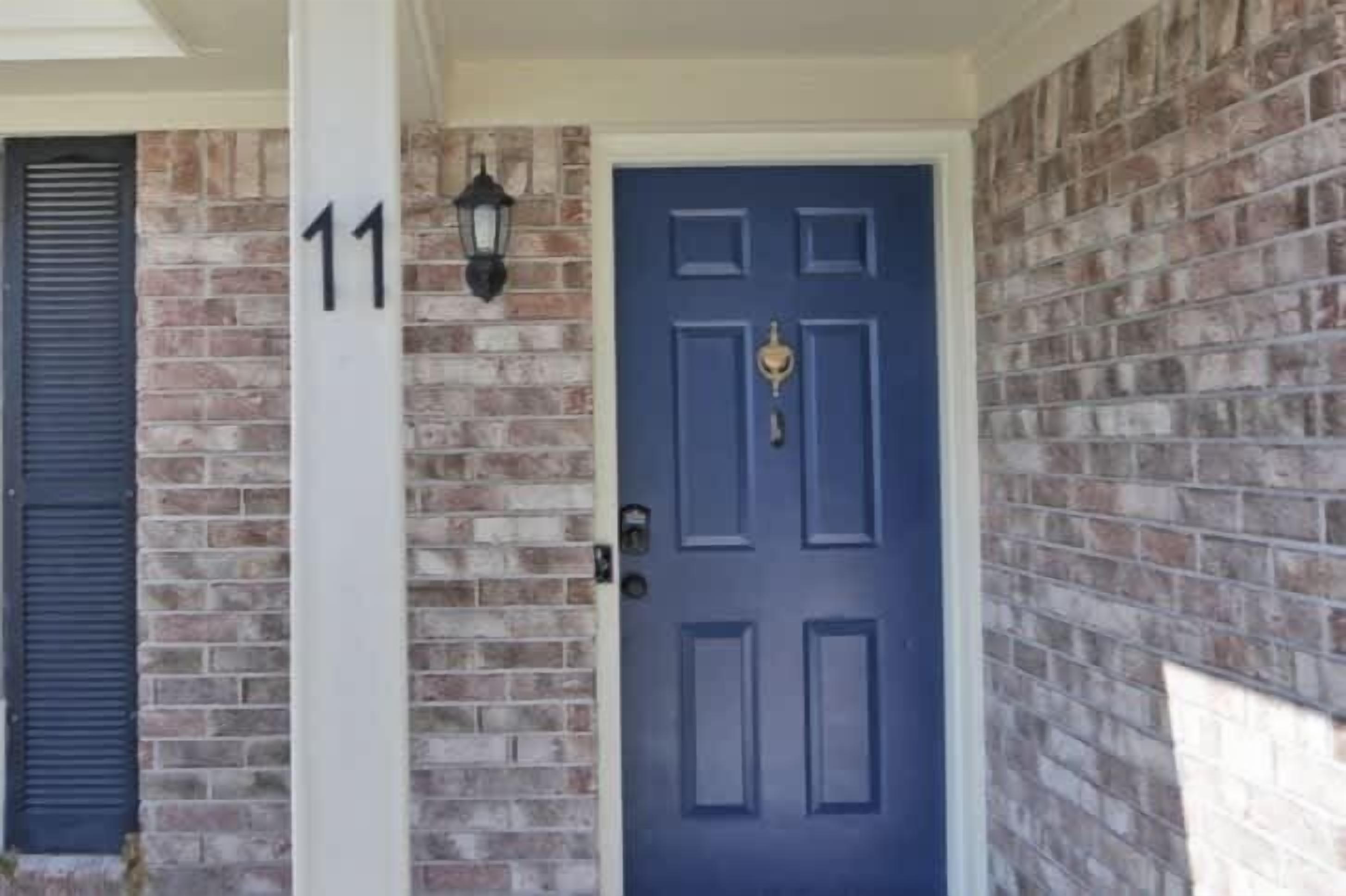Une façade en briques avec une porte bleue, une plaque portant le numéro « 11 » et un luminaire fixé au mur.