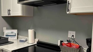A kitchen with white cabinets, a stainless steel microwave, a black stovetop, and a built-in oven. - The Blue Dolphin (Beaufort)