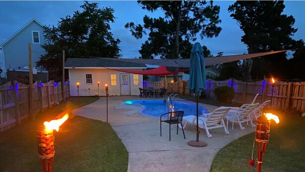 A backyard with a pool, lounge chairs, and tiki torches. - The Blue Dolphin (Beaufort)