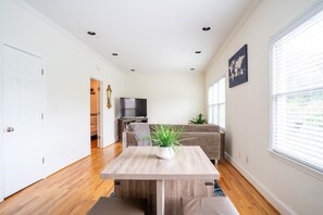 A modern living room with a wooden dining table, a sofa, and a TV in the background.