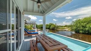 Un espacio exterior cubierto con piscina, mobiliario de madera y vistas a una casa y al agua.