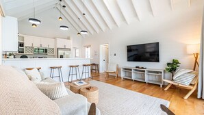 Amplia sala de estar con un televisor grande, piso de madera y una cocina moderna al fondo.