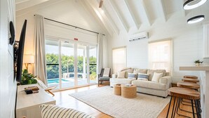 Amplia sala de estar con un sofá grande, una mesa de centro y una zona de bar con taburetes. Posee una puerta corrediza de vidrio que da a un balcón con piscina.