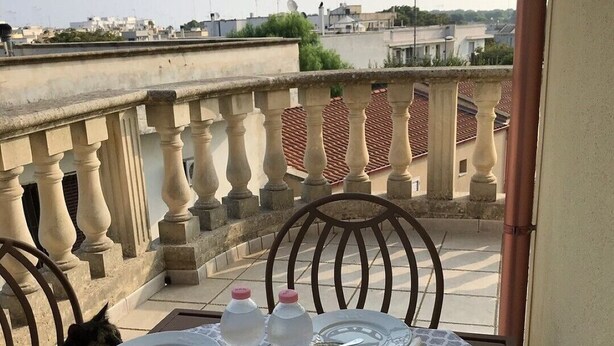 A balcony table set with breakfast items, including croissants, pastries, and beverages, overlooking a cityscape. - Villa Striari - 5 (Puglia)