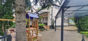 Relax in a serene outdoor space with a play structure, adjacent to a lush garden and a tree.