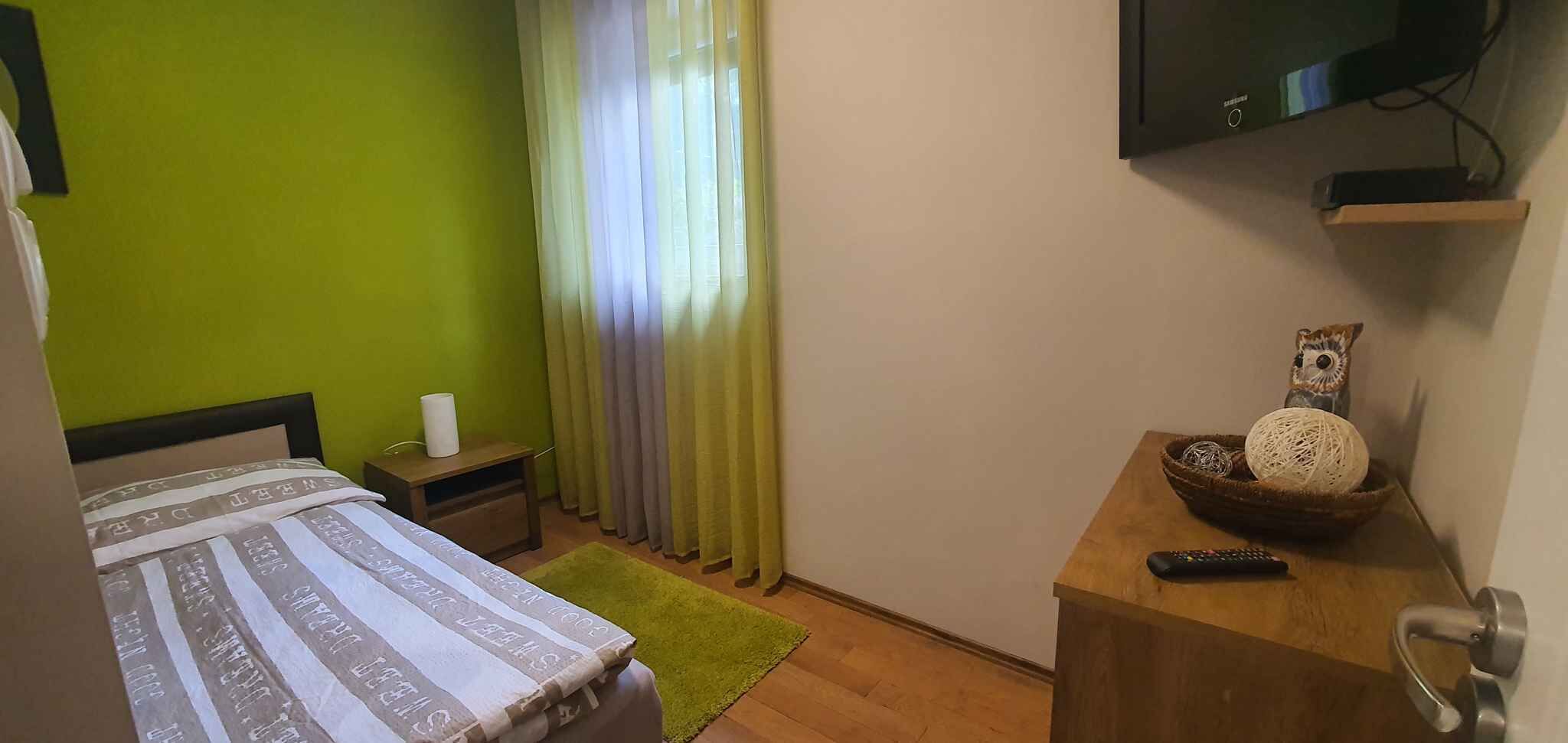 A small, cozy hotel room with a bed, a nightstand, a TV, and a small table with decorative items.