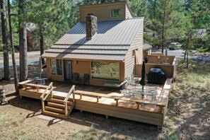 A cabin with a deck, outdoor seating, and a grill area.