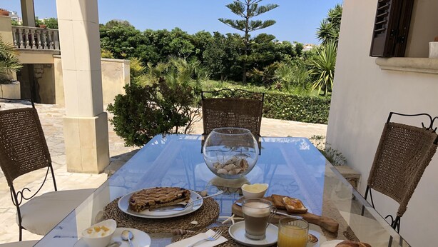 A table set for breakfast with a glass table, wicker chairs, and a view of greenery.