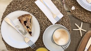 A breakfast setting with croissants, a slice of pie, a glass of orange juice, and a cup of coffee on a woven table.