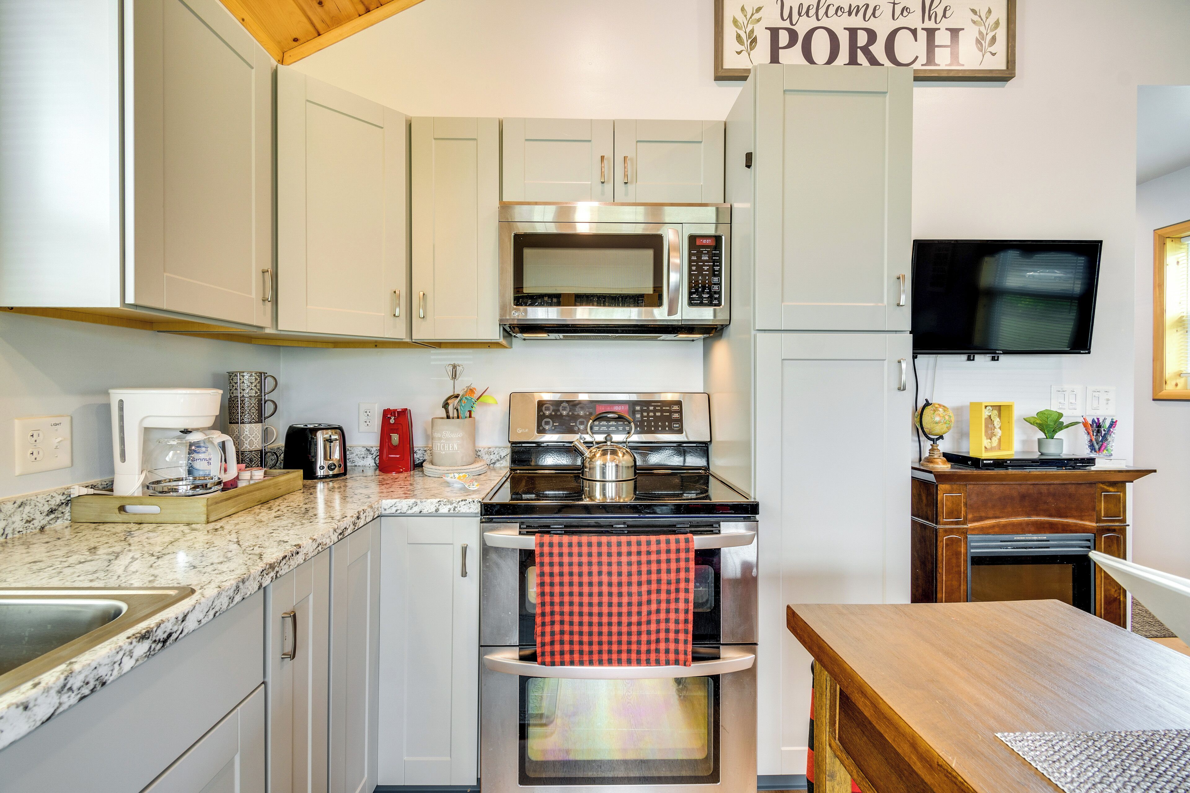 A modern kitchen with stainless steel appliances, a wooden table, and a TV mounted on the wall.