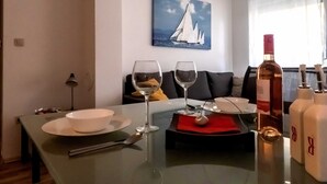 A dining area with a table set for two, a wine glass, a bottle of wine, and a painting of sailboats on the wall.