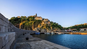 A coastal town with buildings on a hillside, a stone wall, and boats docked at a pier. - Studio mit Klimaanlage Grill (Šilo)