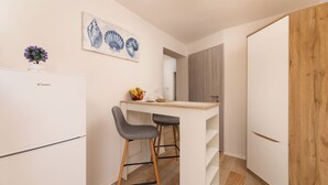 A compact kitchen with a white refrigerator, a wooden cabinet, and two bar stools. - Studio mit Klimaanlage Grill (Šilo)