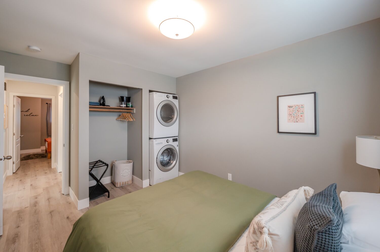 A bedroom with a bed, a washing machine, a laundry basket, and a door leading to a bathroom.
