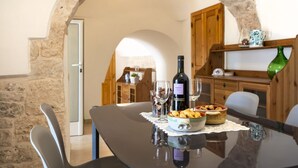 Ein Esstisch mit einer Weinflasche, Gläsern und einer Schüssel Essen in einem steingemauerten Raum, ausgestattet mit Holzschränken und einem Rundbogenportal.