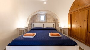 Ein Schlafzimmer mit steinbogiger Nische, einem Bett mit blauer Bettwäsche, zwei Nachttischen mit Lampen und einem Holzschrank.