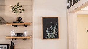 Une cuisine avec des étagères en bois, une estampe botanique encadrée et une pancarte « BIENVENUE » au-dessus de la porte.