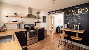 Une cuisine moderne avec des étagères en bois, une cuisinière noire en acier inoxydable et un mur noir ardoise sur lequel est écrit : « BIENVENUE À LA BRASSERIE WEST END ».