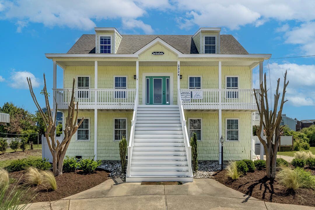 A two-story house with a front porch, a green door, and a staircase leading to the entrance.