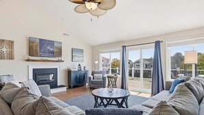 Ein Wohnzimmer mit einer Couch, einem Kamin, einem Deckenventilator und Blick durch große Fenster.