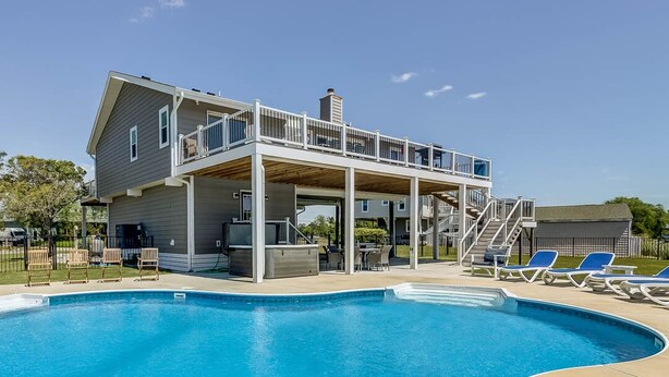 Ein zweistöckiges Haus mit Pool, Sitzgelegenheiten im Freien und einer überdachten Terrasse.