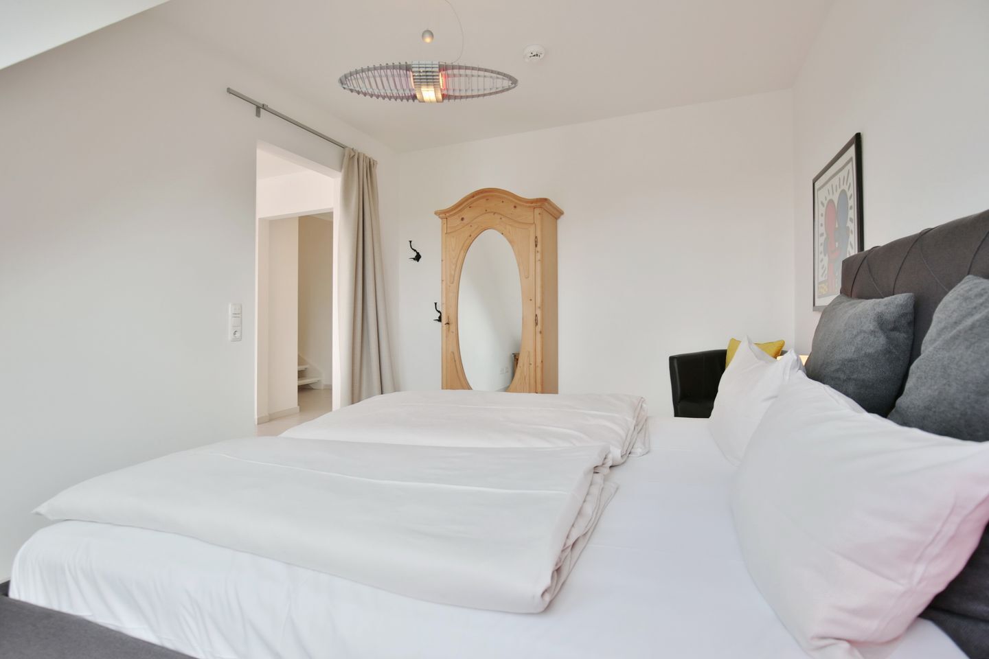 A bedroom with a large bed, a wooden door, a ceiling light fixture, and a framed picture on the wall.
