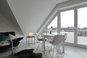 Quarto moderno no estilo loft, com teto inclinado, janelas amplas, mesa de jantar e um espaço de estar aconchegante.
