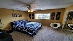 Un dormitorio con cama, ventilador de techo, ventana y una silla.